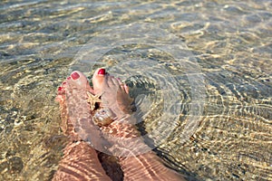 Women`s feet with a pedicure, which are under the water on the beach