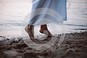 Women& x27;s feet in the river. Close-up side view of a young woman& x27;s bare feet on a sandy river beach at sunset