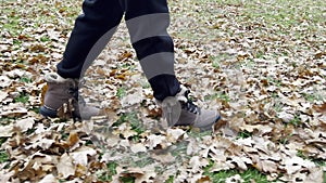 Women\'s feet, shod in winter boots, walk along the fallen leaves lying on the green grass