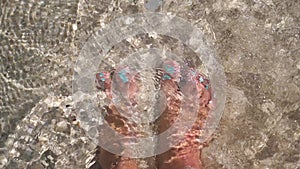 Women`s feet splashing in sea clear water on tropical beach. slow motion