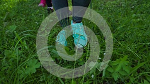 Women`s feet walking on the grass in sneakers. Stock. Outdoor sports on a summer day