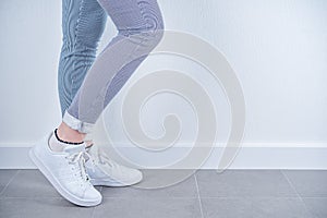 Women`s feet in white sneakers on a white background