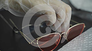 Women's gloved hands put set of sunglasses with colored lenses on table.