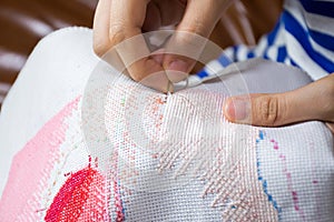 Women`s hand doing cross-stitching with needle