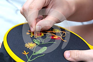 Women`s hand embroidery in a hoop, a woman embroider a pattern on dark material. Close-up. The concept of needlework, hobby,