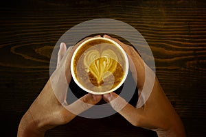 Women`s Hand holding cup of cappuccino coffee with heart shape latte art on old wood table Background, Latte coffee on old wooden