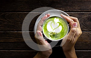 Women`s Hand holding cup of matcha Latte on old Wooden Background table, Green Tea on old Wooden Background table