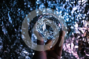 Women`s hand holding a fortune teller crystal ball and looking into the future. Blurred sparkly light background, backdrop shown