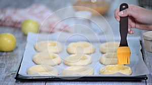 Women`s hand lubricate the buns with egg. Cooking open buns with apple Vatrushka - traditional Russian baking. Series