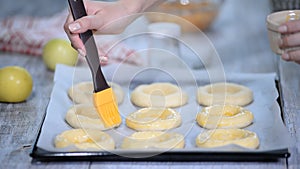 Women`s hand lubricate the buns with egg. Cooking open buns with apple Vatrushka - traditional Russian baking. Series.