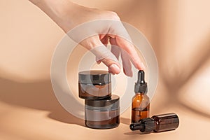 Women& x27;s hand takes bottle of amber glass with cosmetic serum on beige background. Mockup of containers with dropper
