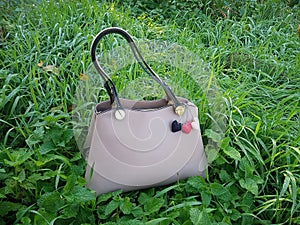 Women\'s handbag stands on the grass with dew. The object is decorated with knitted hearts.