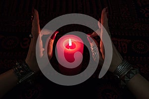 Women`s hands with bracelets and rings holding a burning candle in the dark.