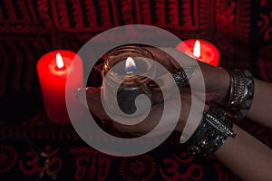 Women`s hands with bracelets and rings holding a burning candle in the dark.