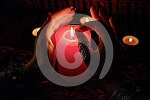 Women`s hands with bracelets and rings holding a burning candle in the dark.