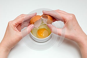 Women`s hands breaking a raw egg into a white cup standing on a white background