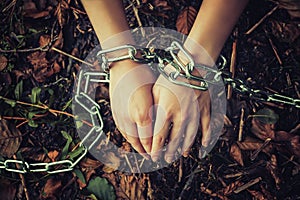 Women`s hands chained in a dark forest - the concept of violence, hostage, slavery