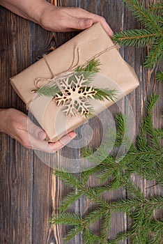 Women`s hands with a Christmas gift in craft paper with a fir branch, snowflake on a brown wooden