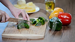 Women`s hands cut green pepper on a wooden Board