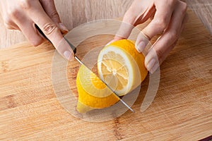 Women`s hands cuting a lemon in half on the wooden cutting board