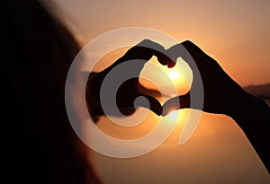 Women`s hands in the form of a heart against the sky pass the sun`s rays. Hands in the shape of a heart of love