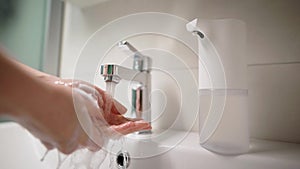 Women`s hands in the frame. The girl used an automatic dispenser for soap. The foam generator has put the right volume.