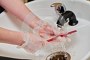 Women& x27;s hands in hair coloring gloves wash a comb under a stream of water in a white sink