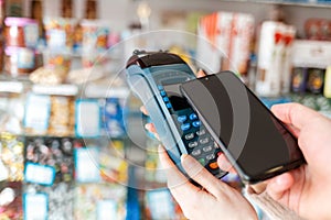 Women`s hands are held by a payment terminal and a man pays for a purchase using a smartphone. Copy space. The concept of NFC,