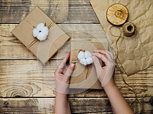 Women`s hands hold a box on a wooden background.The decor is made of cotton flowers.Christmas, birthday