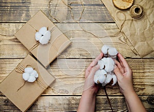Women`s hands hold a box on a wooden background.The decor is made of cotton flowers.Christmas, birthday