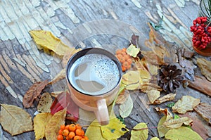 Women`s hands hold a cup of hot drink, Autumn, fall leaves, hot steaming cup of coffee and a warm scarf on wooden table