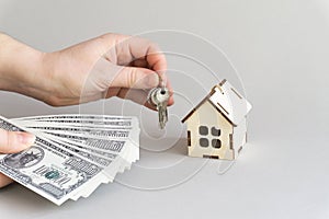 Women`s hands hold dollars and keys to a miniature house on a gray monochrome background, a place to copy. The concept