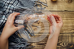 Women `s hands hold a glass bottle with a garland of Christmas lights .Warm grey scarf or plaid on a wooden background