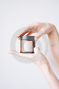 Women's hands hold glass jar with empty label on light background, mockup