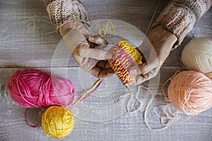 Women`s hands hold knitting needles and a colorful thread to ti