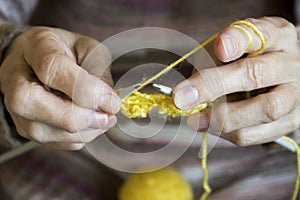 Women`s hands hold knitting needles and a yellow thread to tie