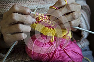 Women`s hands hold knitting needles and a yellow thread to tie