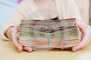 women& x27;s hands hold a stack of rubles tied with a rubber band.