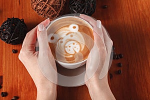 Women`s hands holding a Cup of coffee with a painted Teddy bear latte art. Vintage color. Coffee shop concept