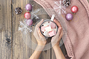 Women`s hands holding cup with hot coffee with foam and marshmallows on of wooden table.The concept of winter, warmth, holidays