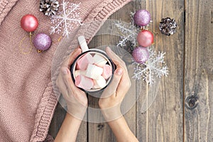 Women`s hands holding cup with hot coffee with foam and marshmallows on of wooden table.The concept of winter, warmth, holidays
