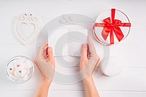 Women`s hands holding empty greeting card on white background with romantic decoration as giftbox, frame in shape of heart, angel