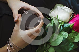 Women`s hands are holding a glass of tea, there are roses nearby. Lifestyle concept