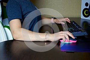 Women`s hands on the keyboard and gaming mouse. Female gamer playing computer games, side view. Gaming keyboard and mouse