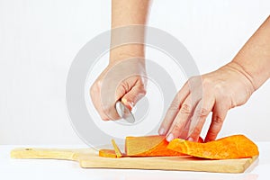 Women's hands with a knife chops carrot on a cutting board