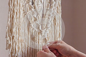 Women`s hands knit knots of cords in a macrame panel