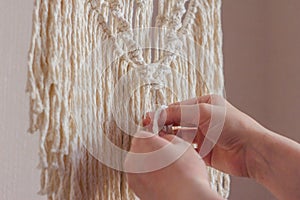 Women`s hands knit knots of cords in a macrame panel