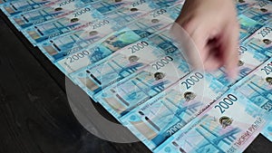 Women`s hands lay out 2000-ruble Russian bills in even rows on a dark vintage table. Money background