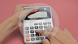 Women`s hands make a count on a calculator on a pink background close-up.