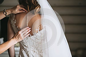 Women`s hands mother corrected dress on the back of a bride with a beautiful embroidered veil and buttons